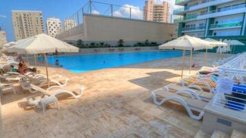 A poolside area with lounge chairs and umbrellas, a swimming pool, and high-rise buildings in the background.