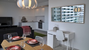 A modern living room with a dining area, a kitchen, and a view of a high-rise building. - Modern Seaview Apartment In a Prime Location (Sliema)