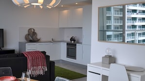 A modern kitchen with white cabinets, a dining area with a wooden table set for four, and a large window overlooking a residential area. - Modern Seaview Apartment In a Prime Location (Sliema)