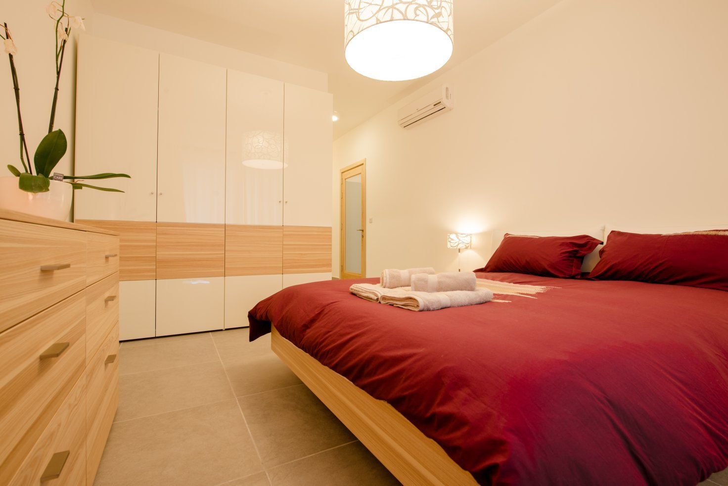 A modern bedroom with a wooden bed, a wardrobe, and a nightstand with a lamp.
