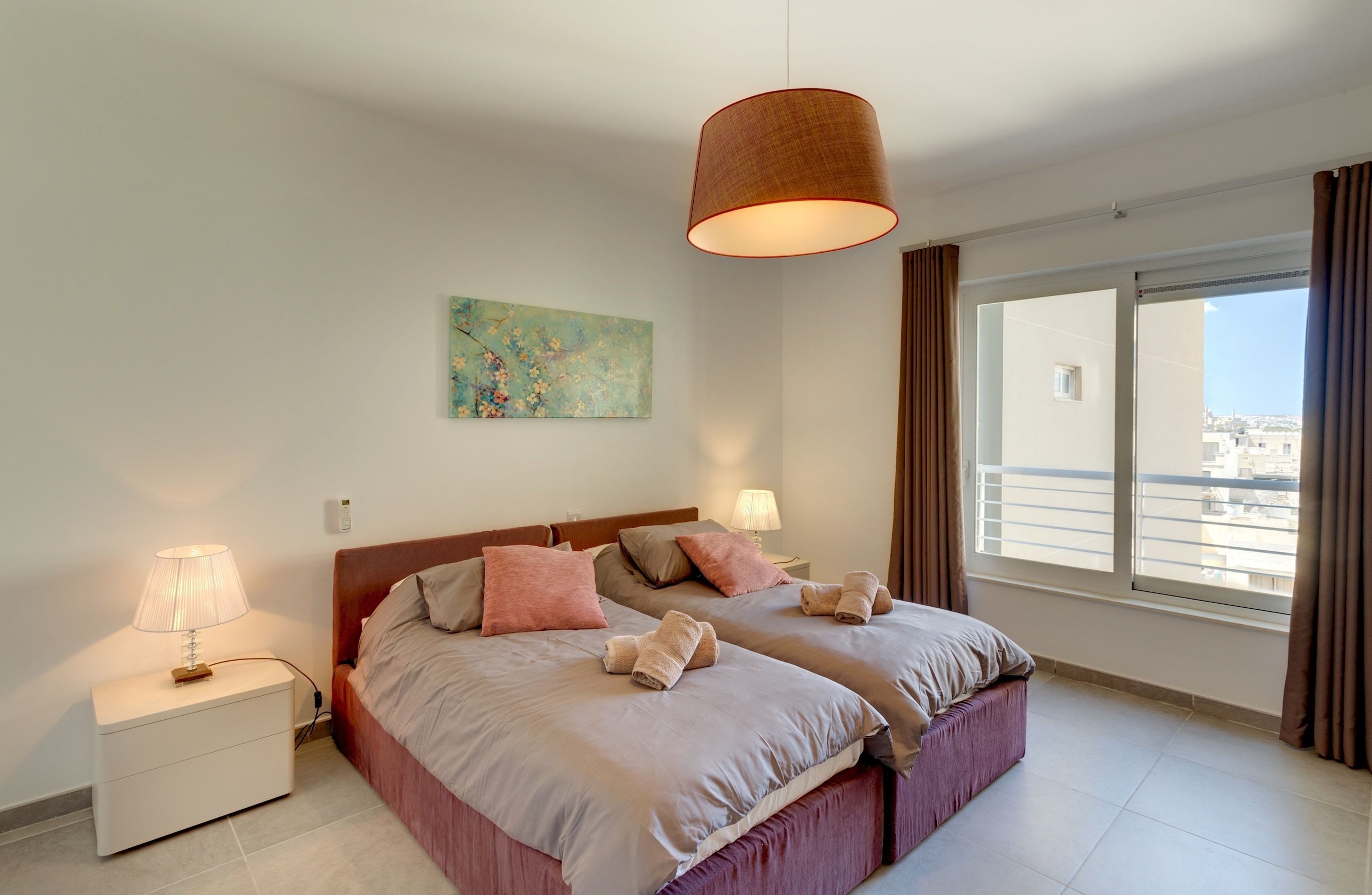 Un lit double avec deux oreillers, une table de chevet avec une lampe et une fenêtre avec des rideaux.
