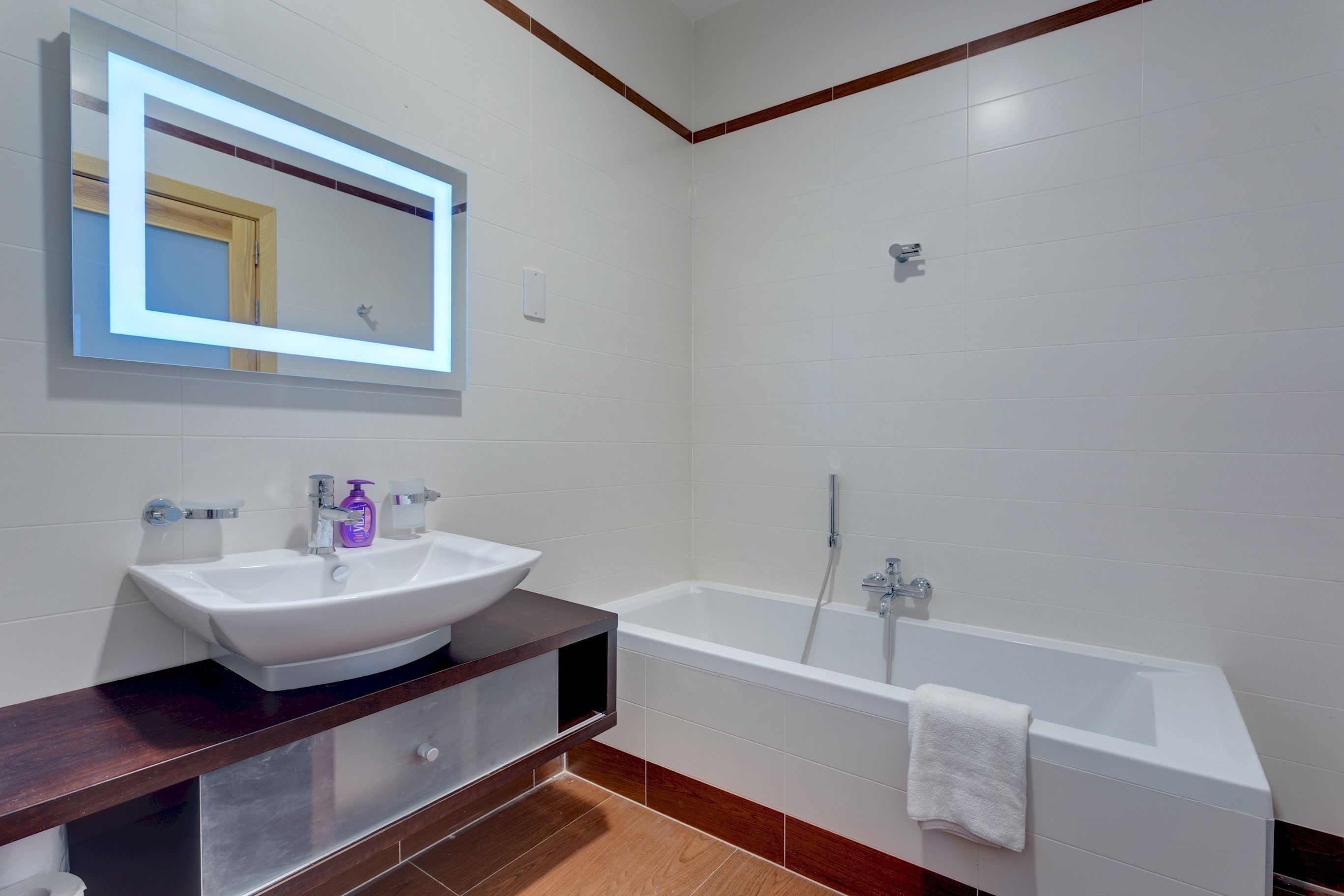 A modern bathroom with a white sink, vanity, and bathtub.