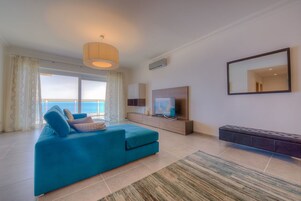 Ein modernes Wohnzimmer mit einer großen Couch, einem Fernseher und einem Balkon mit Meerblick.