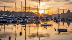 A marina with multiple boats docked, a prominent dome structure in the background, and calm water reflecting the sunset. - Seafront Apart IN Fort Cambridge (Sliema)