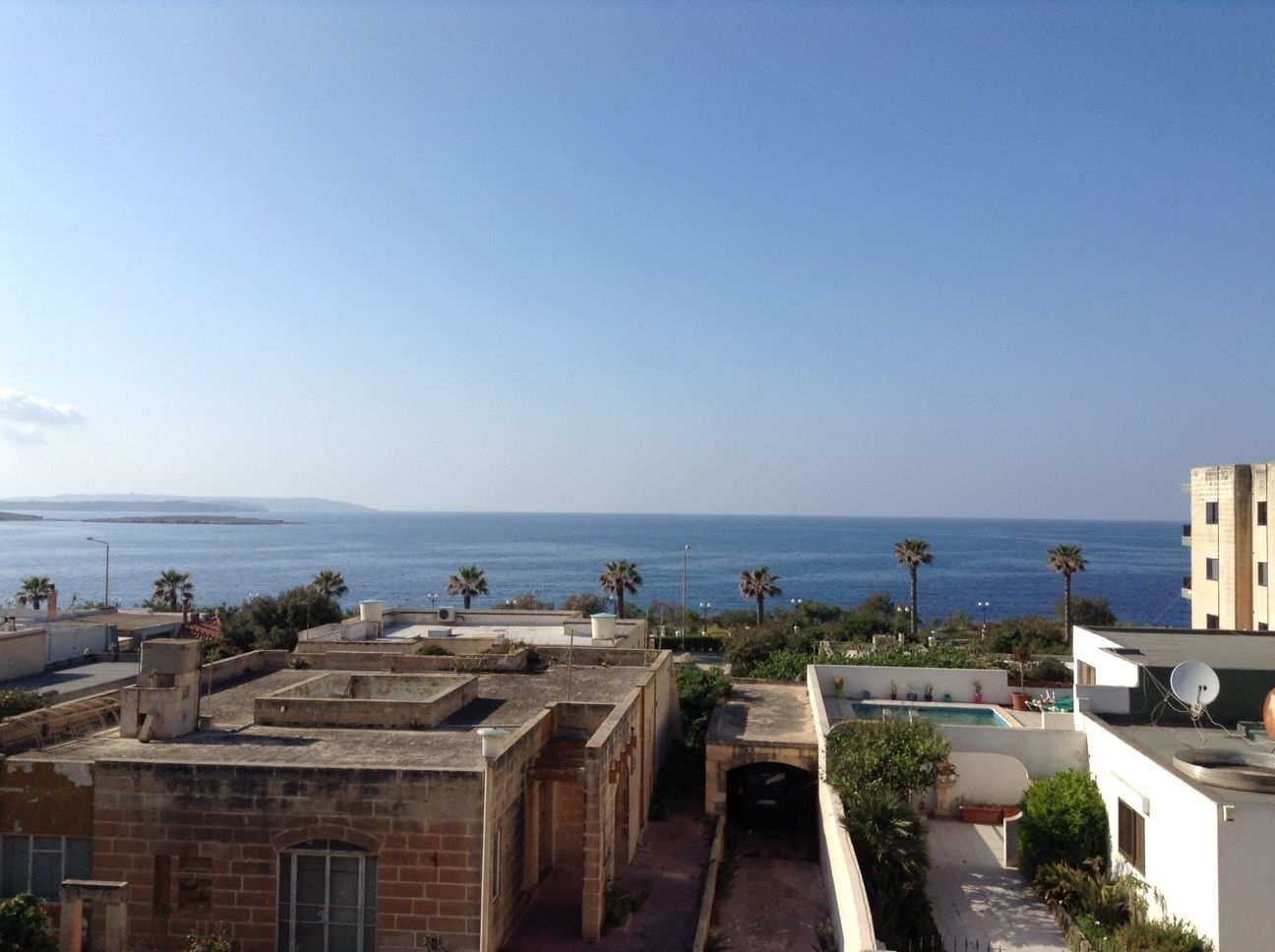A coastal residential area with buildings, a clear sky, and a view of the sea.