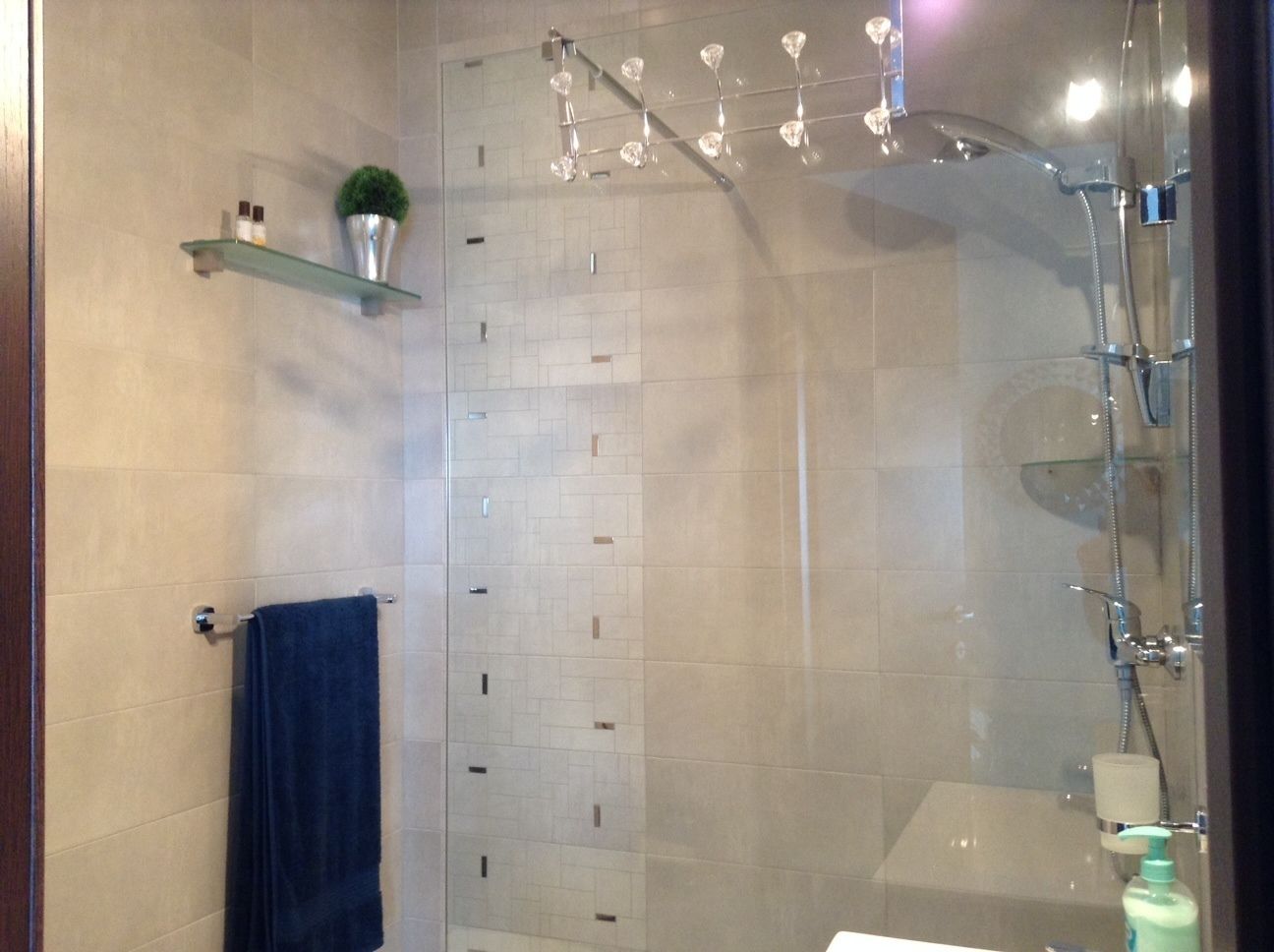 A modern bathroom with a glass shower enclosure, a towel rack, and a shelf with toiletries.