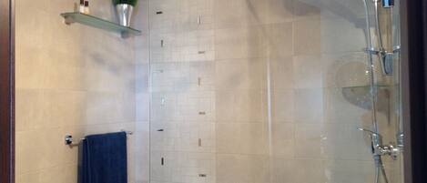 A modern bathroom with a glass shower enclosure, a towel rack, and a shelf with toiletries.