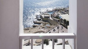 A view from a window overlooking a coastal area with a clear sky, a sun shining, and a beach with buildings and a pool. - Seafront Apartment, Marvelous Views GR8 Location (Sliema)