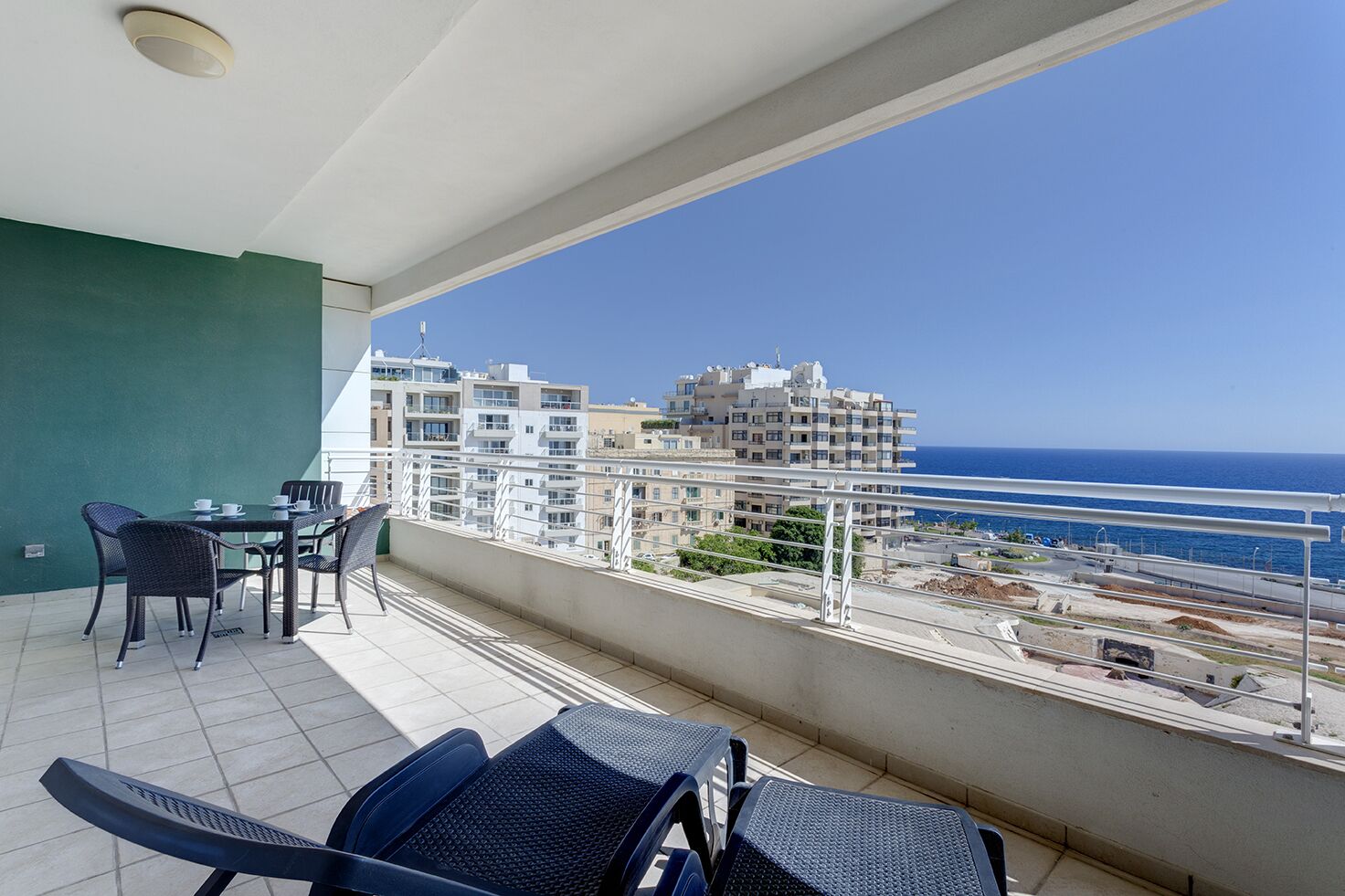 A balcony with a table and chairs, a view of the sea, and buildings in the background.