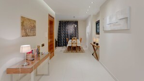Um corredor com área de jantar, com mesa e cadeiras, luminária e obras de arte nas paredes.