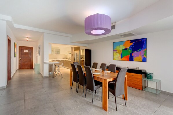 A modern dining area with a wooden table and chairs, a kitchen in the background, and a colorful abstract painting on the wall. - Seaview Apartment In Fort Cambridge, Sliema (Sliema)