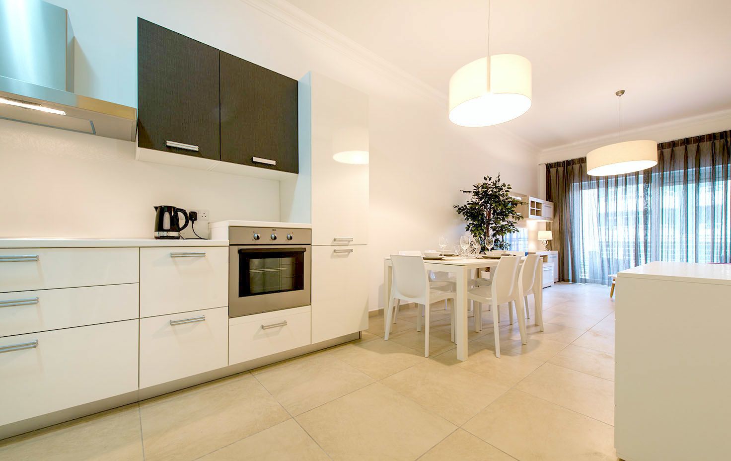 Een moderne keuken met witte kastjes, een inbouwoven en een eethoek met een tafel en stoelen.