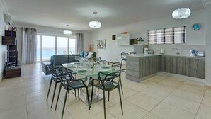 A modern kitchen with a central island, a dining area with a glass table and chairs, and a view of the sea through large windows. - Stunning Seafront Lux Apt wt Pool, Upmarket Area (Sliema)