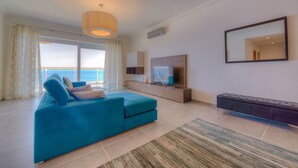 Un salon moderne avec un grand canapé, un téléviseur et un balcon offrant une vue sur la mer.