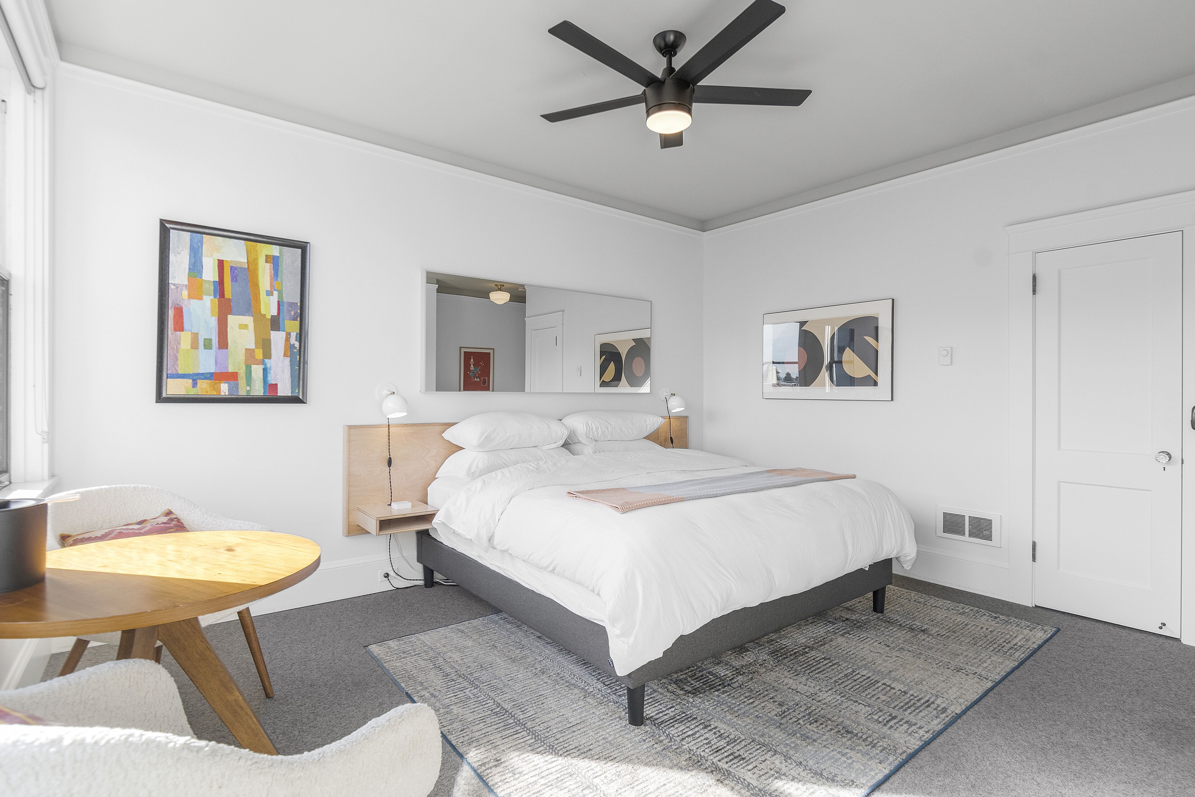 A modern bedroom with a bed, bedside tables, a round table, and a ceiling fan.