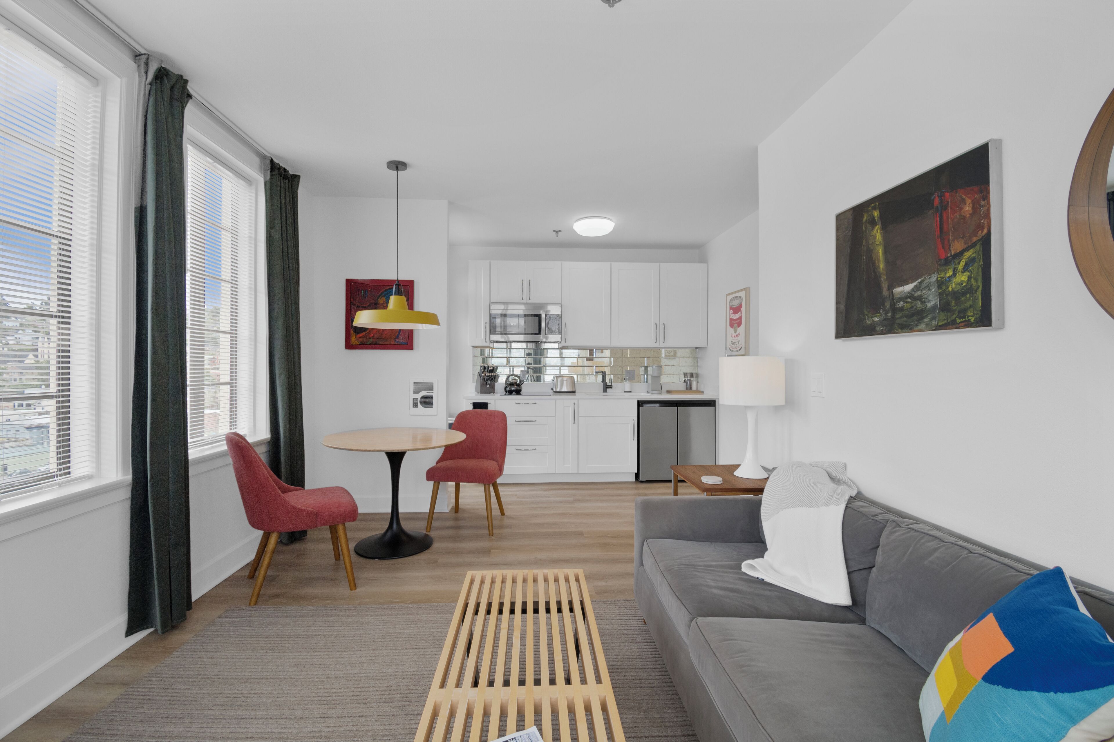 A modern living room with a grey sofa, red chairs, a wooden coffee table, and a city view through large windows.