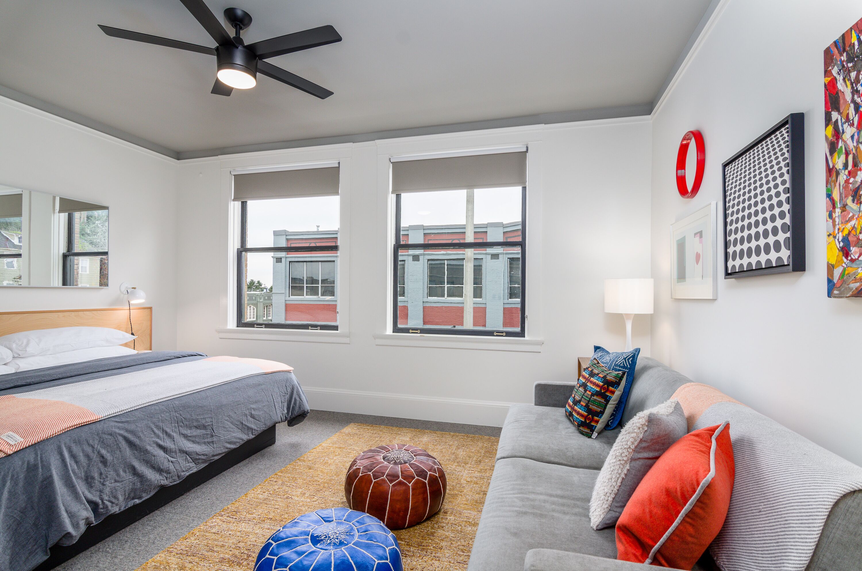 Quarto moderno com cama, sofá, ventilador de teto e janelas amplas.