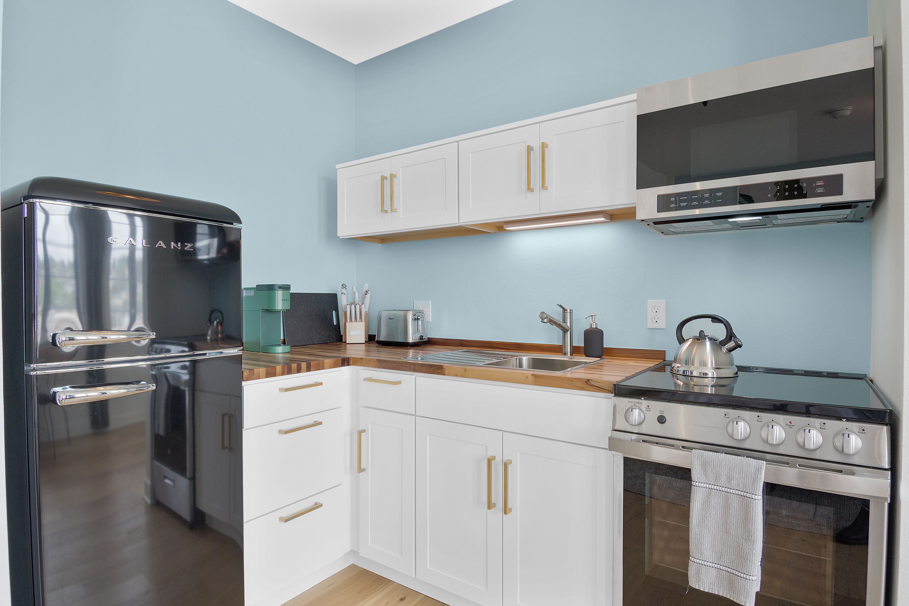 A modern kitchen with white cabinets, stainless steel appliances, and a wooden countertop.