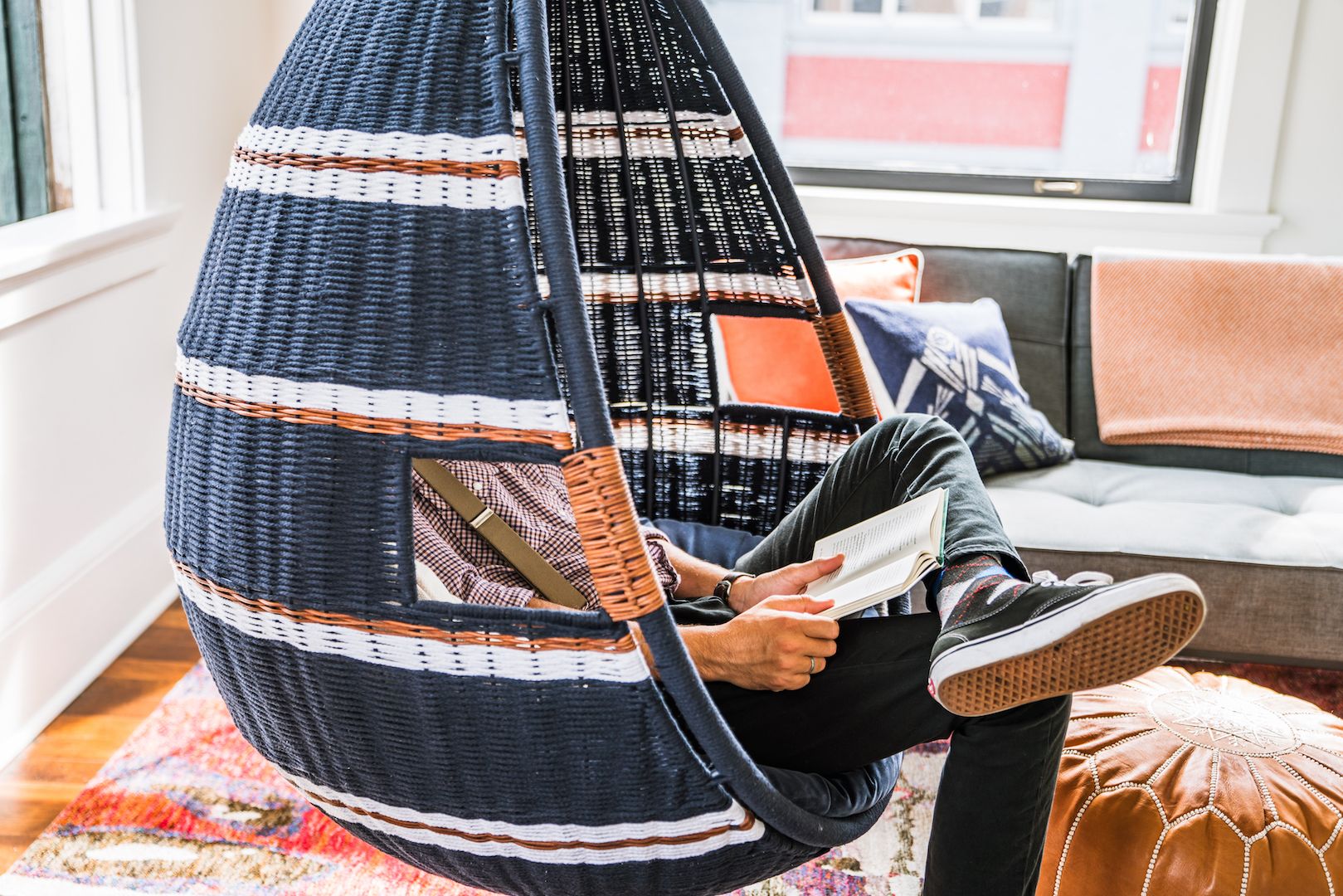 A person sitting in a hanging chair with a woven seat and backrest, reading a book.