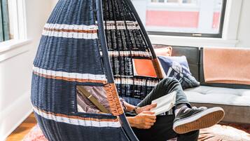A person sitting in a hanging chair with a woven seat and backrest, reading a book.