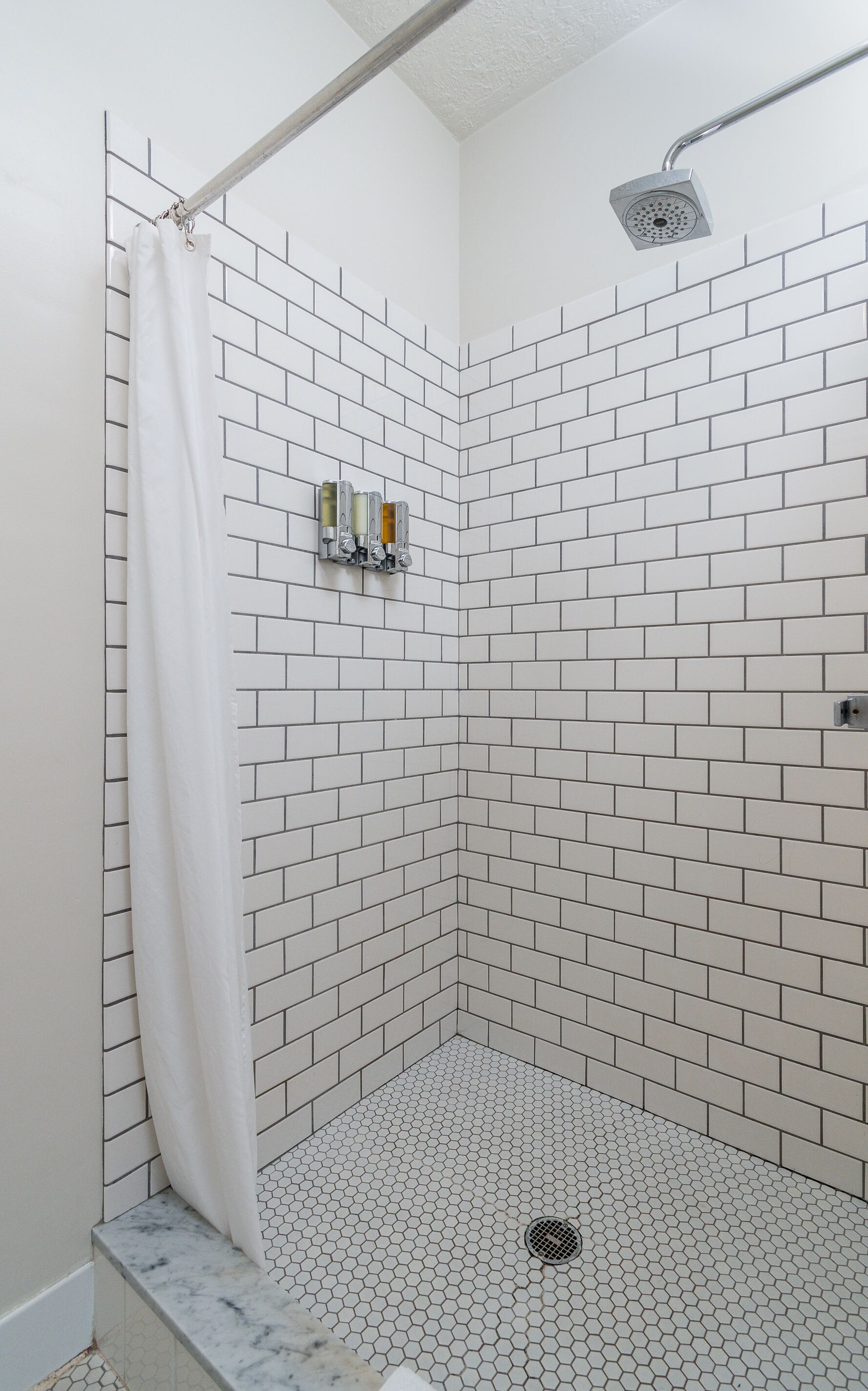 Eine Dusche mit weißen, sechseckigen Fliesen, einem Duschkopf und einem Vorhang.