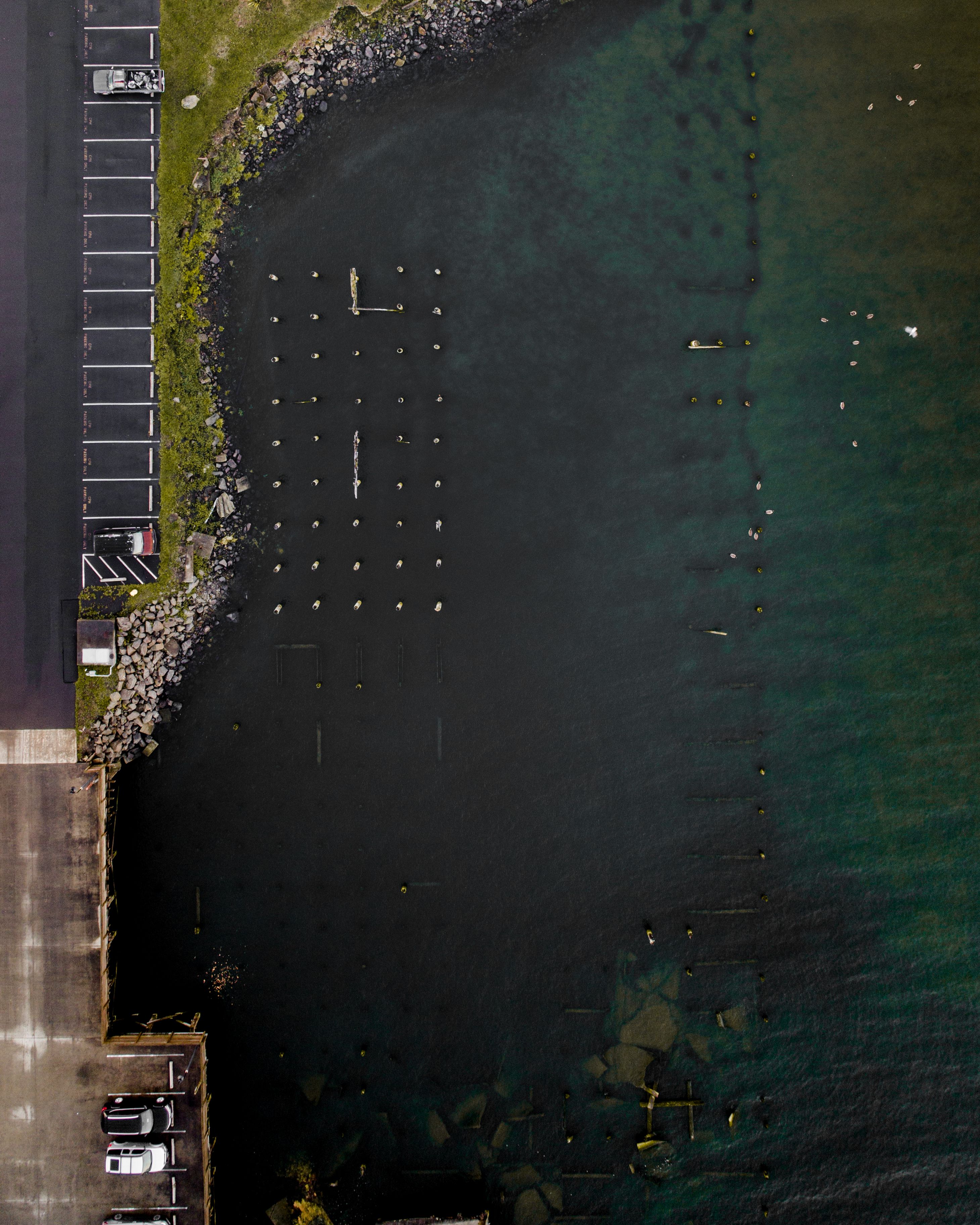 An aerial view of a parking area adjacent to a body of water with clear water and a rocky shoreline.