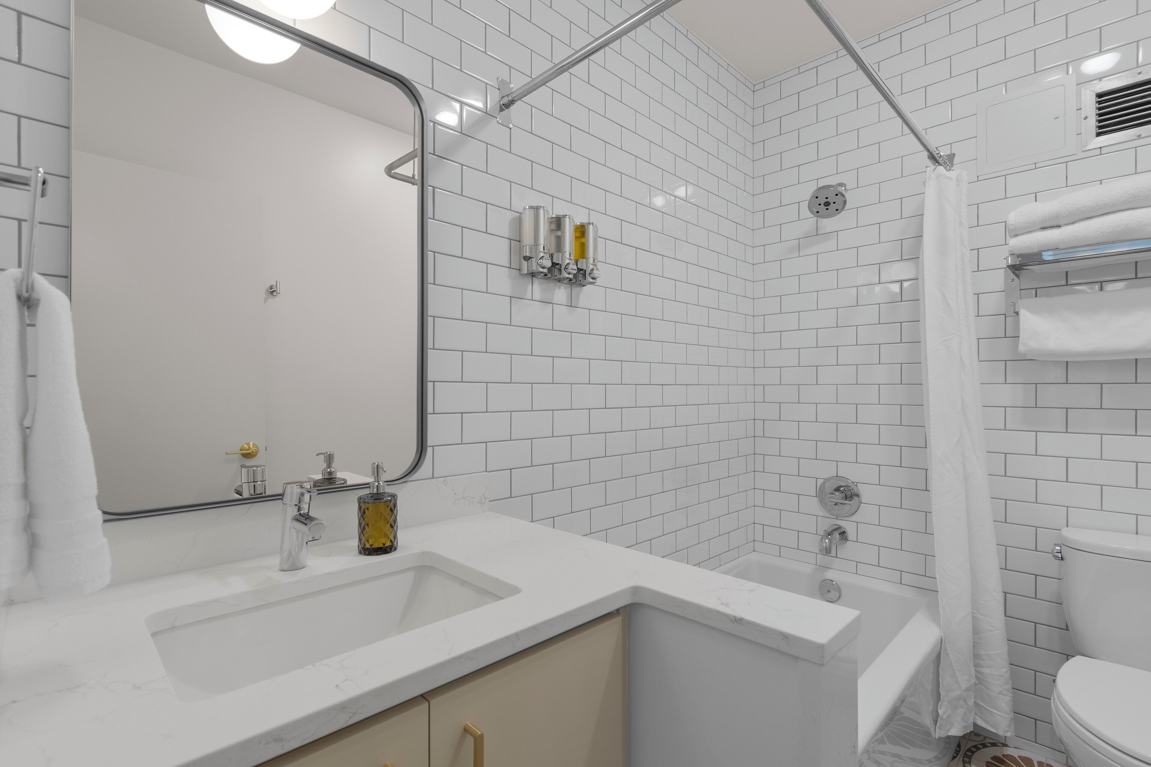 A modern bathroom with white subway tiles, a large mirror, a bathtub, and a toilet.