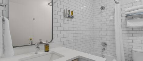 A modern bathroom with white subway tiles, a large mirror, a bathtub, and a toilet.