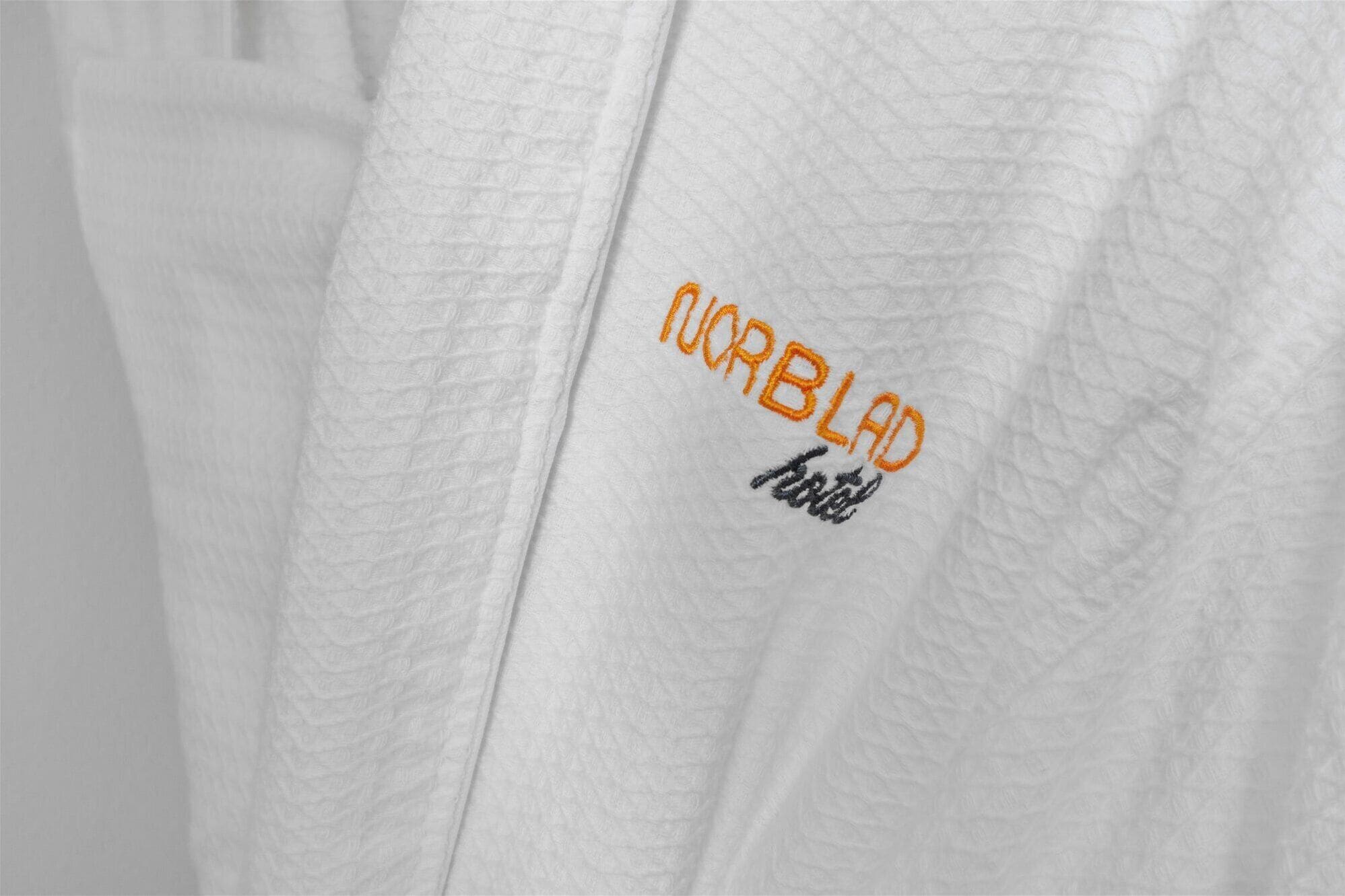A white textured fabric with embroidered text "CORBLAD" and a smaller text below it.