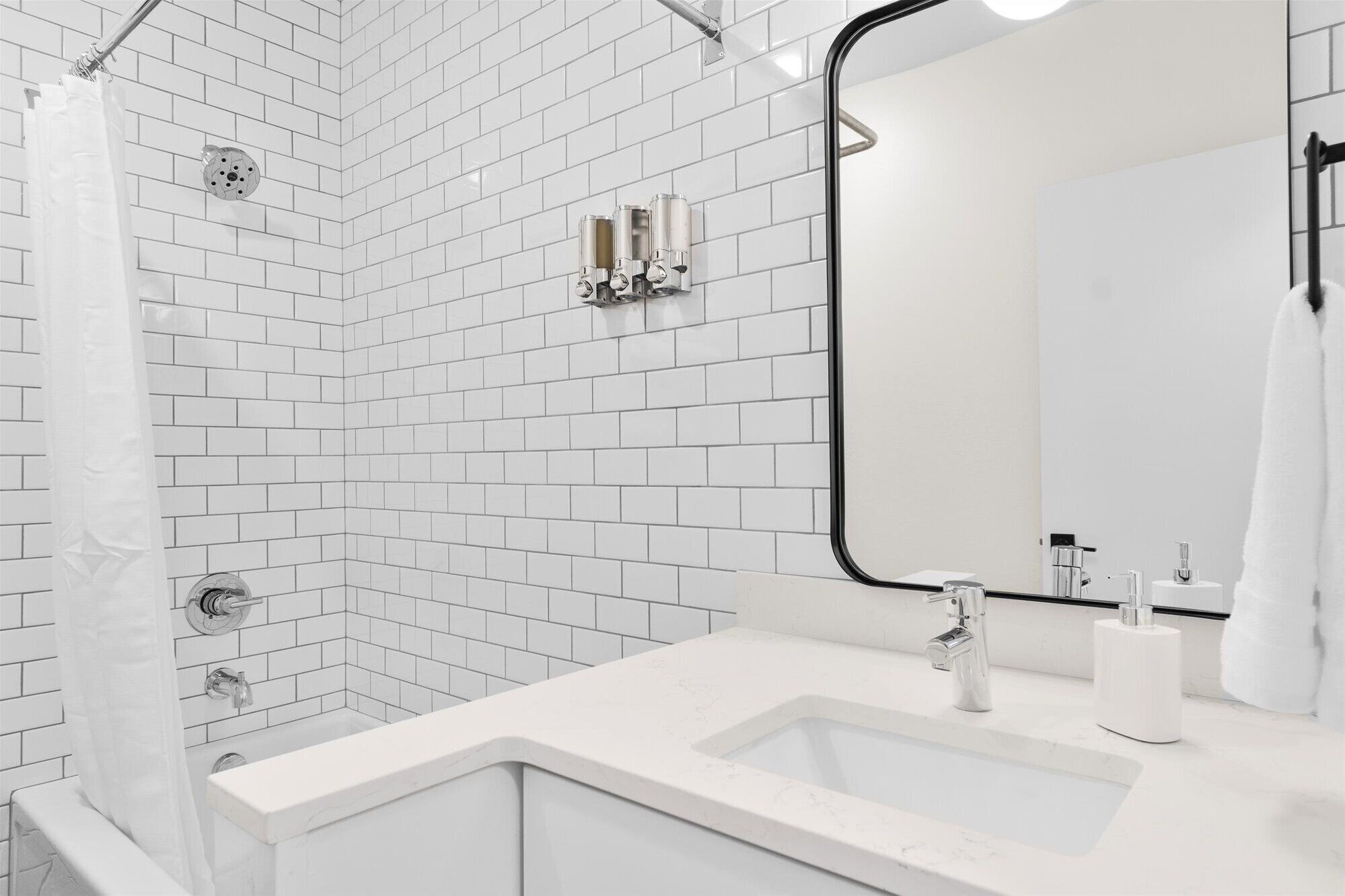 Uma casa de banho moderna com azulejos brancos tipo metrô, um espelho grande, chuveiro com cortina e lavatório branco com torneira.