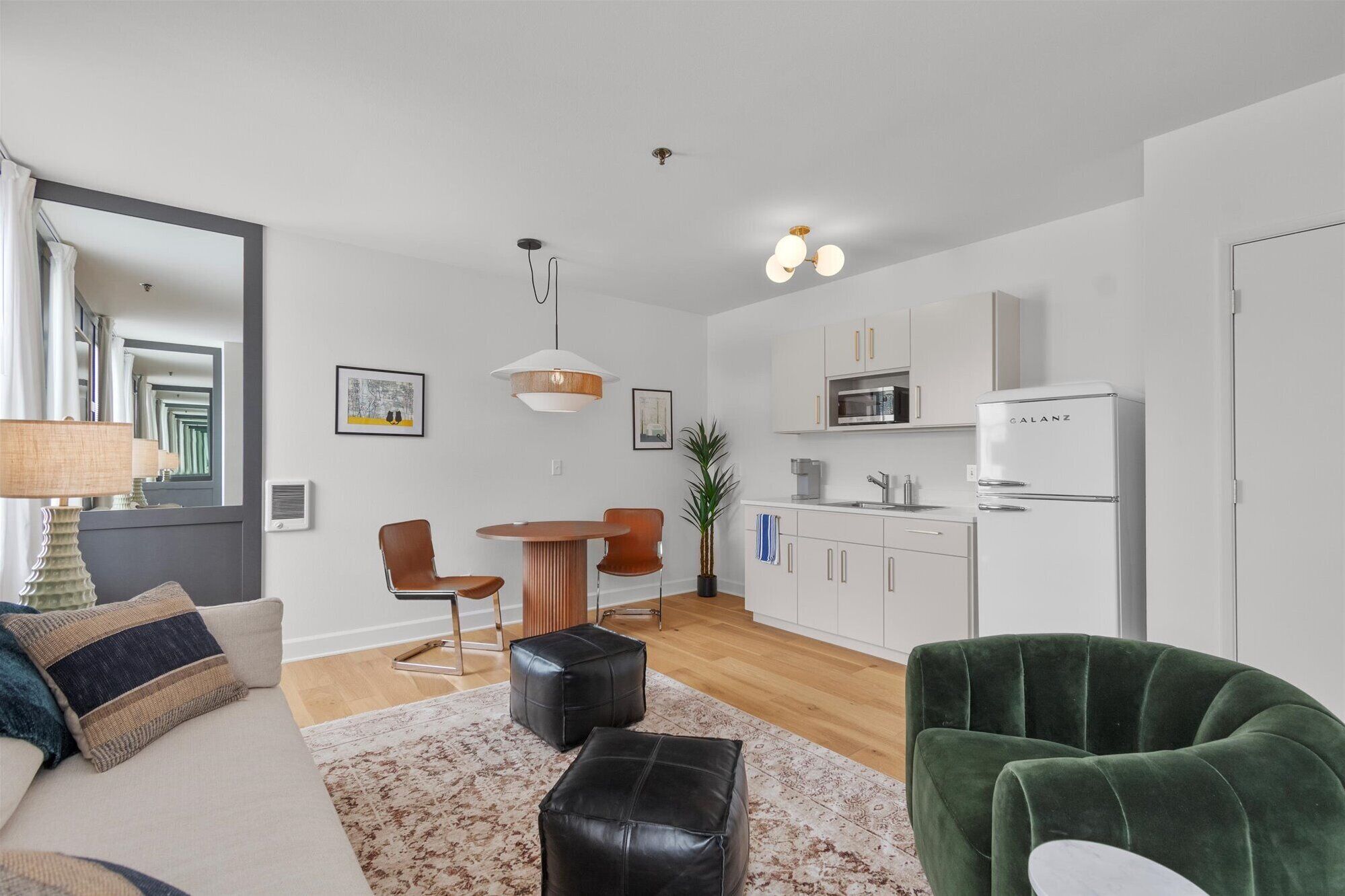 A modern living room with a sofa, two chairs, a coffee table, and a green armchair. There is a kitchen area with a microwave, refrigerator, and cabinets.