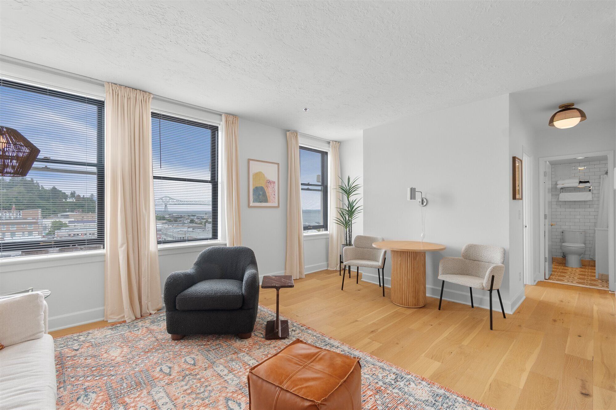 A modern living room with a large window, a sofa, a coffee table, and a dining area.