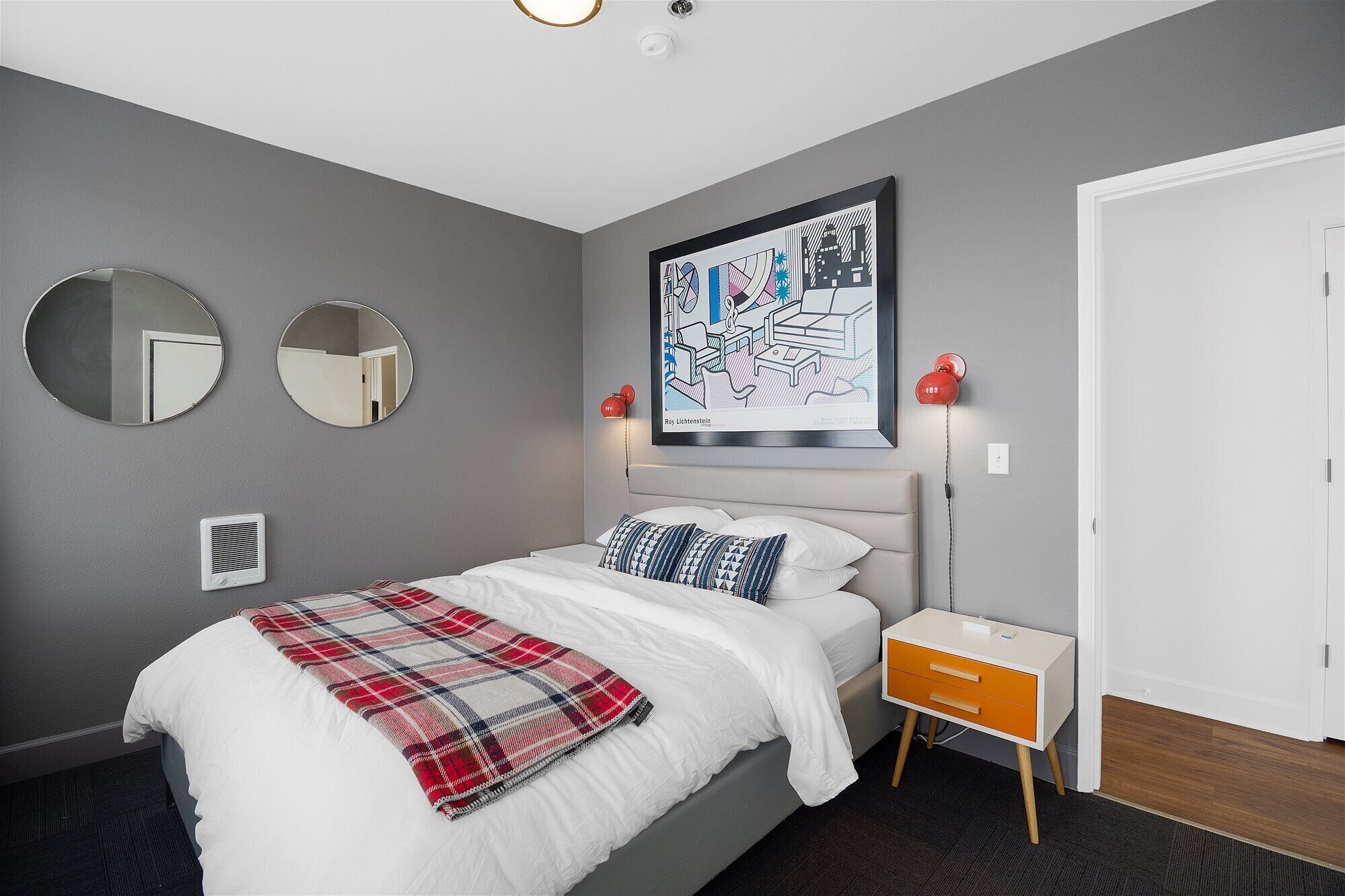 A modern bedroom with a bed, two round mirrors, a red telephone, and a framed artwork on the wall.