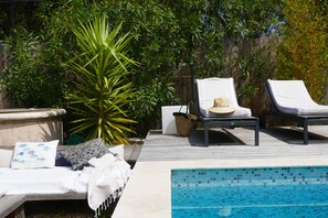Un área junto a la piscina con sillas de descanso, una mesita y una planta decorativa.