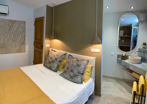 A bedroom with a bed, a bedside table, a mirror, and a wall-mounted light fixture. - La Vagabonde (Saint-Tropez)
