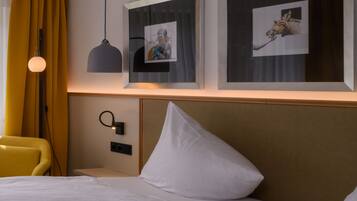 A hotel room with a bed, a bedside table, a lamp, and two framed pictures on the wall.