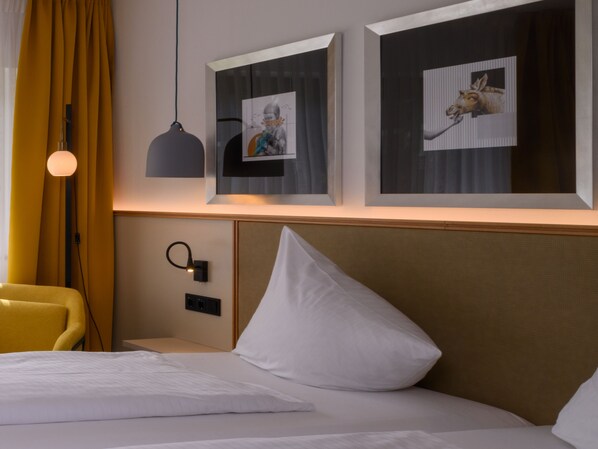 Una habitación de hotel con cama, mesita de noche, lámpara y dos cuadros en la pared.