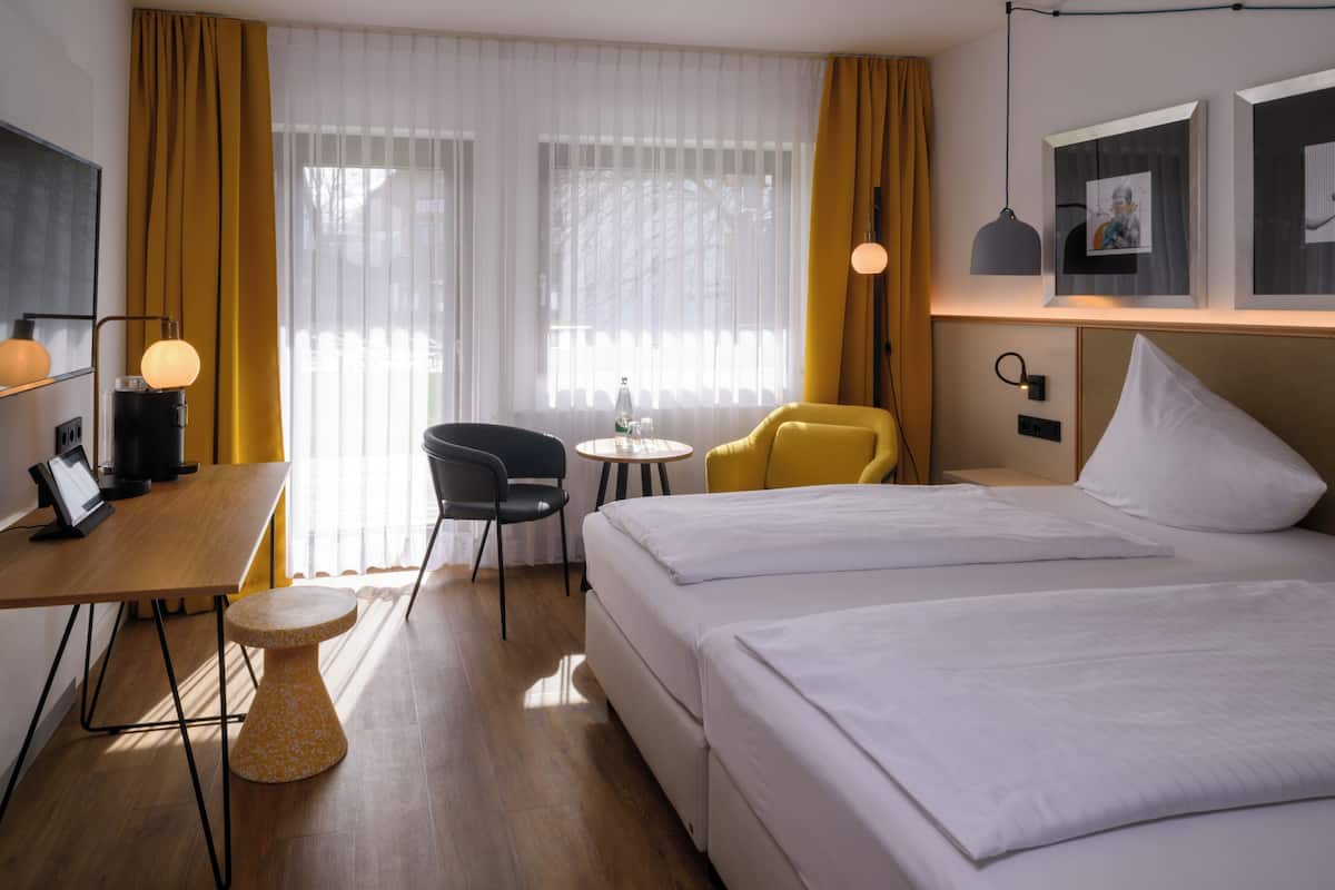 Une chambre d’hôtel comprenant un lit, un bureau, une chaise, une petite table et une lampe.