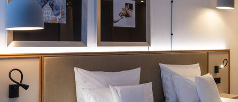 A hotel room with a large bed, two wall-mounted picture frames, and two pendant lights.