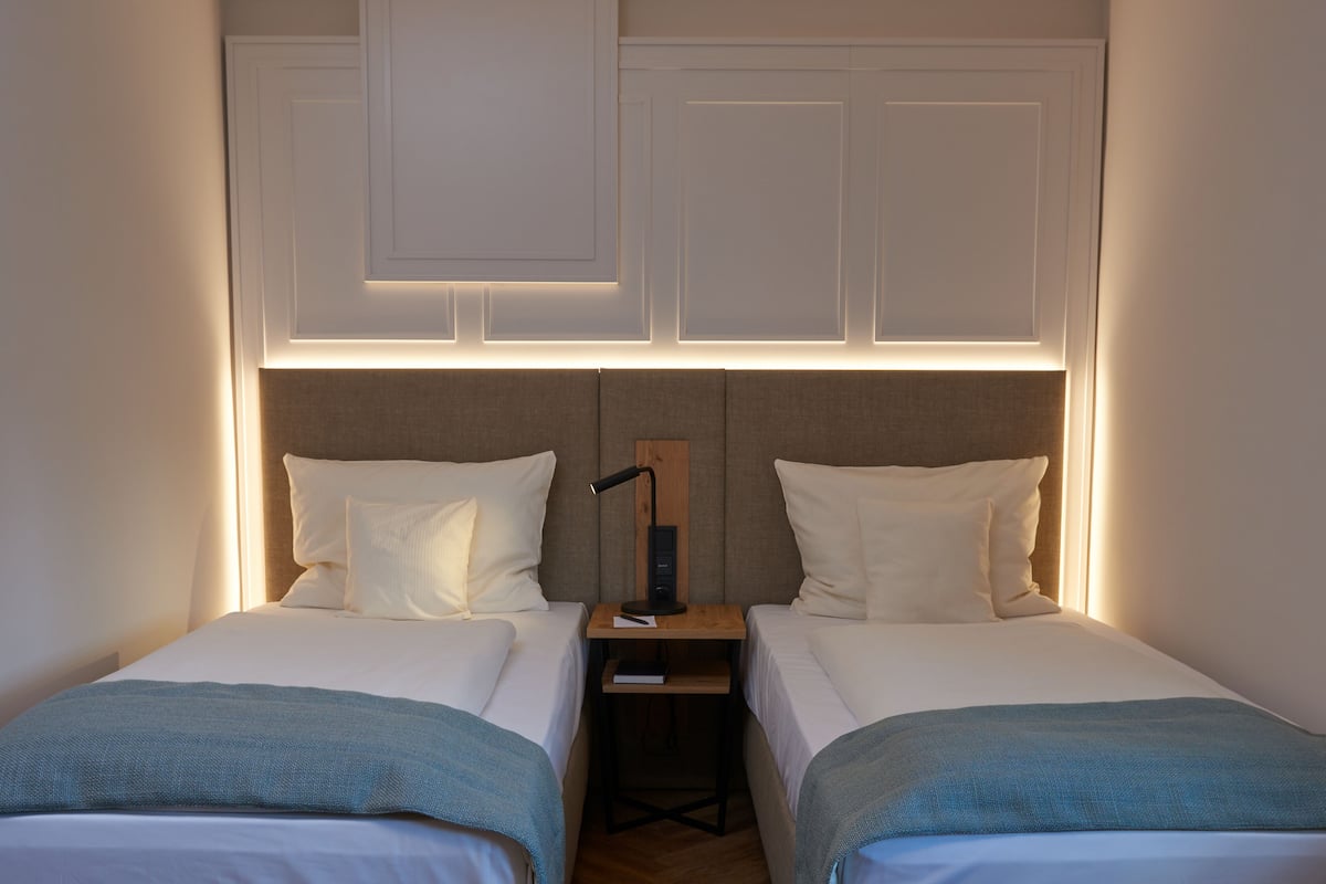 Une chambre avec deux lits, une table de chevet et un luminaire fixé au mur.