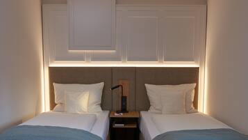 A bedroom with two beds, a nightstand, and a wall-mounted light fixture.