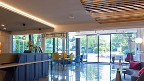 A modern interior with a reception desk, seating area, and large windows offering a view of the outdoors. - Hotel Schnitterhof (Bad Sassendorf)