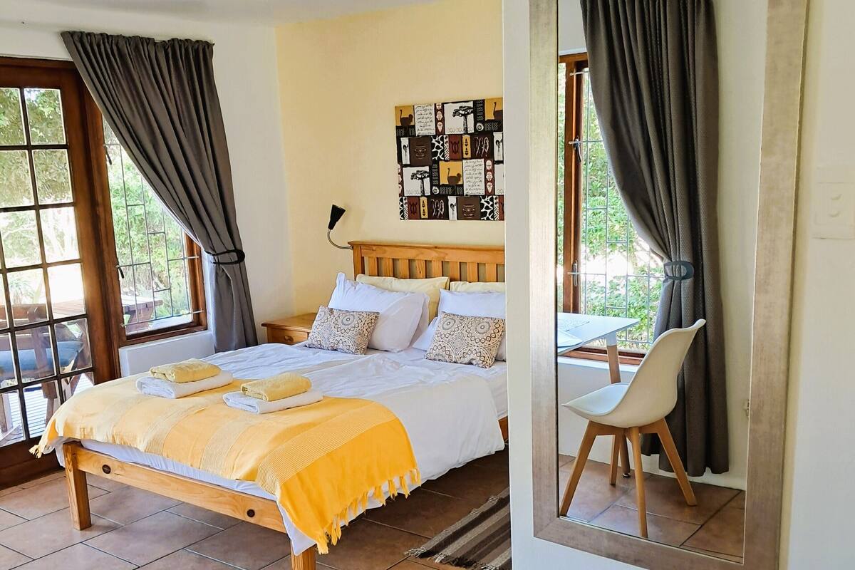 A bedroom with a bed, a chair, a mirror, and a window with curtains.