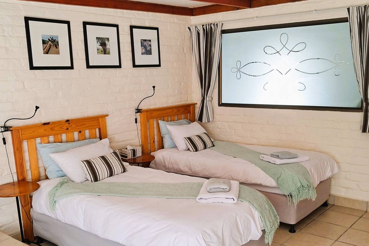 A bedroom with two beds, wooden headboards, a window with curtains, and framed pictures on the wall.