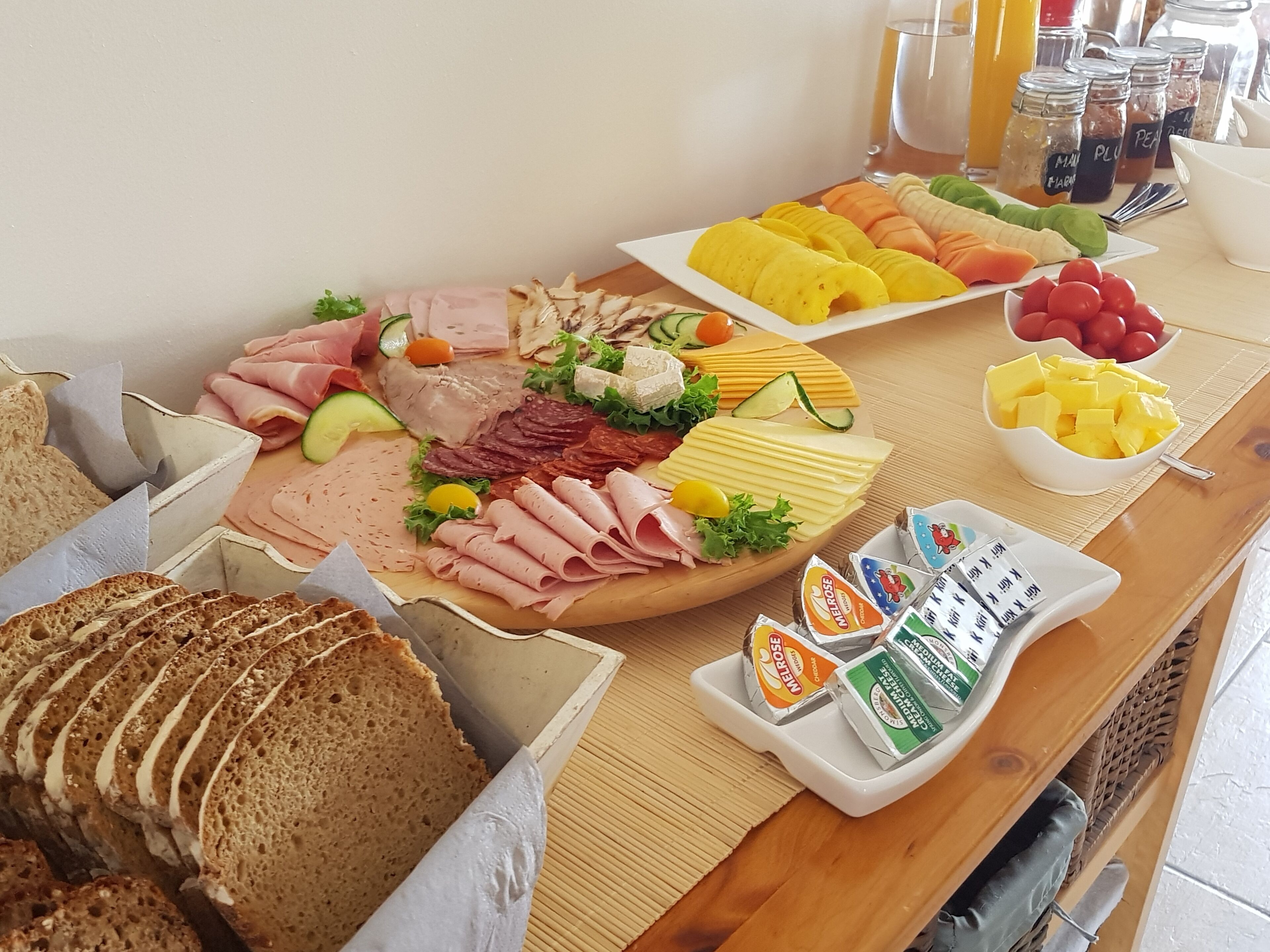 Un bufé de desayuno con diversos embutidos, quesos, frutas y panes.