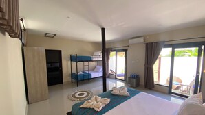 Ein Hotelzimmer mit einem großen Bett, einem Stockbett, einem Schreibtisch und einer Schiebetür zu einem Balkon.