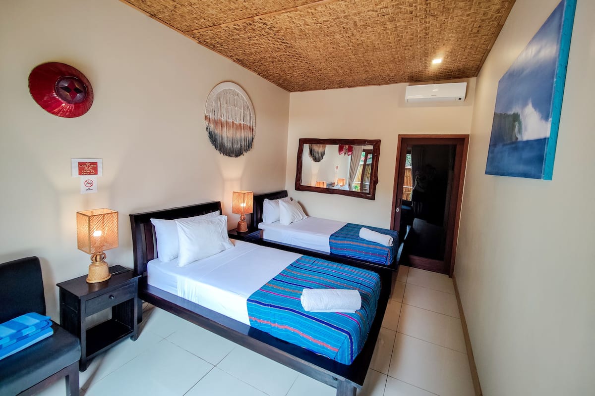 Une chambre d’hôtel avec deux lits, un plafond en bois, un climatiseur fixé au mur, un miroir encadré et un élément décoratif mural.