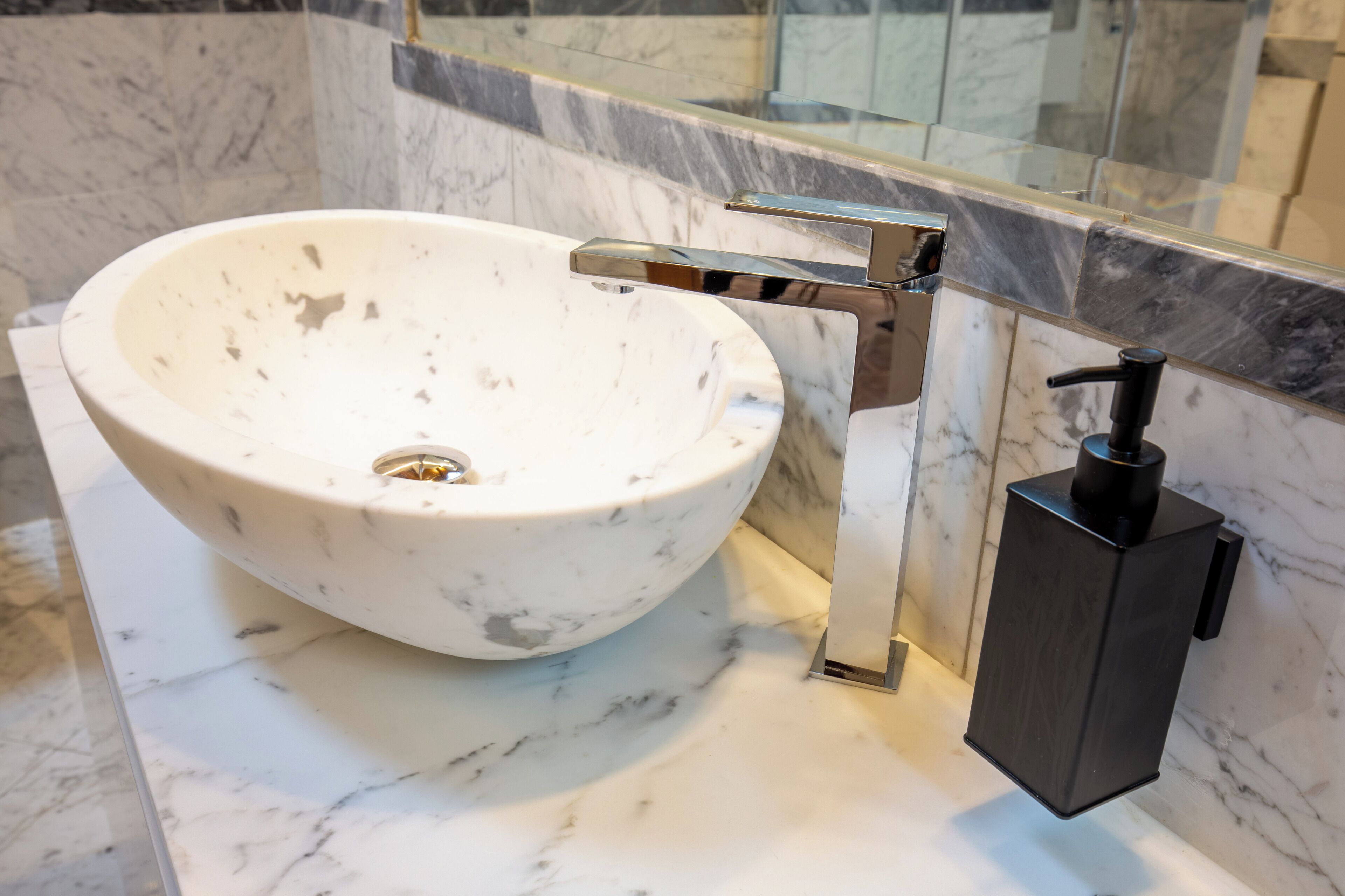 Une salle de bain avec un lavabo en marbre blanc, un robinet chromé et un distributeur de savon noir.