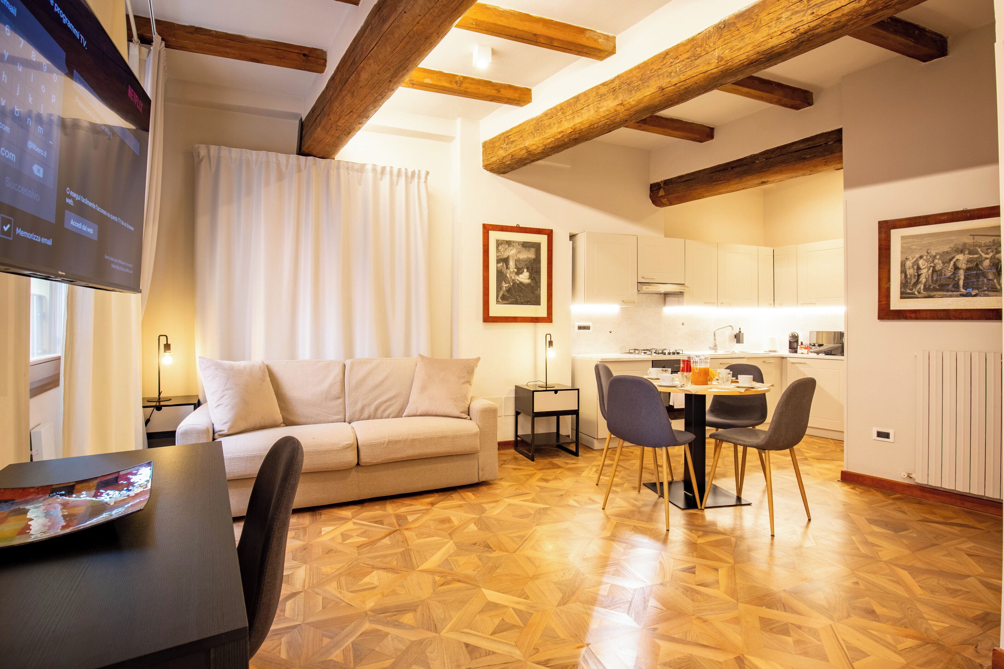 Una sala moderna con un sofá, una mesa de comedor y sillas. Hay una zona de cocina con armarios y una encimera.
