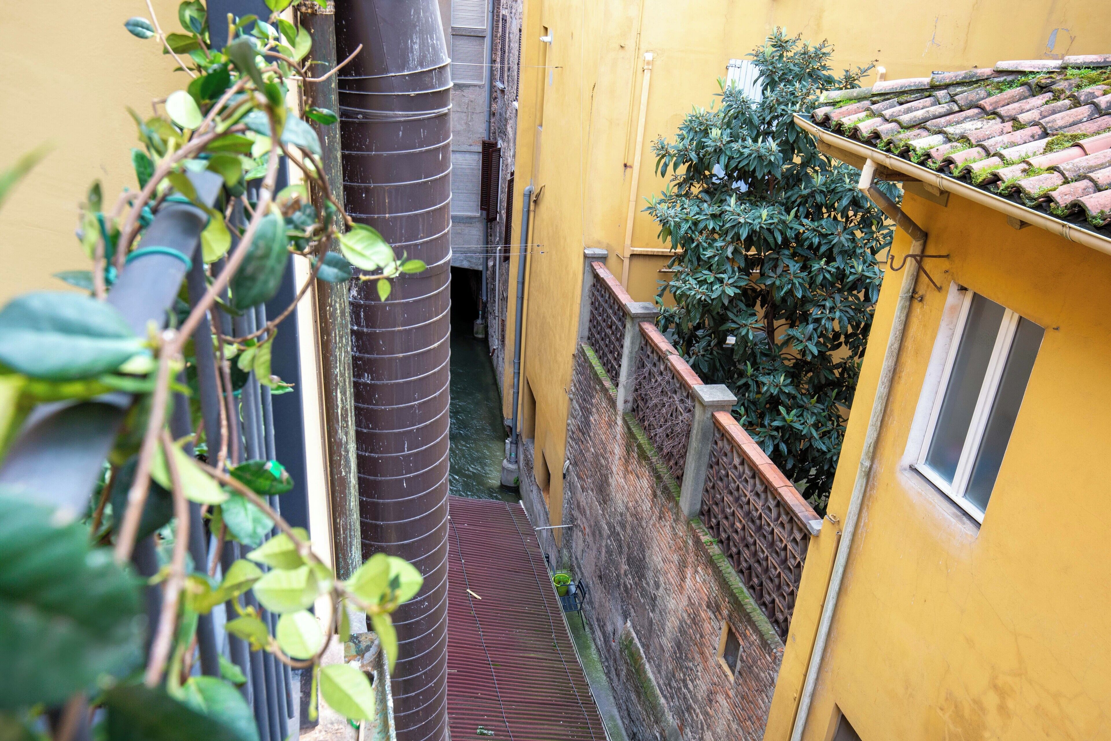 Uma viela estreita com um edifício amarelo de um lado e uma escadaria de metal descendo.